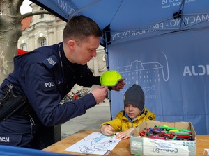 Zdjęcie kolorowe: umundurowany policjant daje dziecku odblaskową czapkę z daszkiem