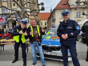 Zdjęcie kolorowe: dwóch umundurowanych policjantów wraz z mężczyzną na tle radiowozu