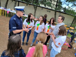 Zdjęcie kolorowe: umundurowany policjant ruchu drogowego rozmawia z grupą młodzieży