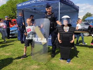 Zdjęcie kolorowe: umundurowana policjantka pozuje do zdjęcia z dwoma chłopcami, którzy mają sprzęt policyjny