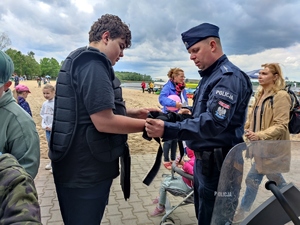 Zdjęcie kolorowe: umundurowany policjant pomaga założyć chłopcu ochraniacze