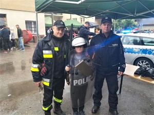 Zdjęcie kolorowe: widoczny strażak Ochotniczej Straży Pożarnej, chłopiec i umundurowany policjant