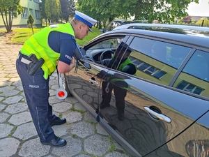 Zdjęcie kolorowe: umundurowany policjant ruchu drogowego stoi przy zatrzymanym samochodzie