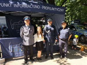 Zdjęcie kolorowe: umundurowani policjanci wraz z dziewczynką pozują do zdjęcia, w tle policyjny namiot profilaktyczny.