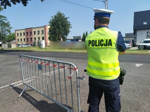 Zdjęcie kolorowe: umundurowany policjant ruchu drogowego podczas zabezpieczenia drogi.