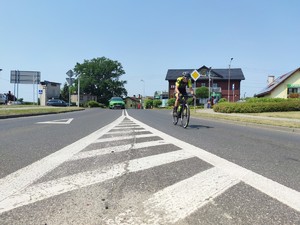 Zdjęcie kolorowe: na pierwszym planie kolarz, w tle samochód.