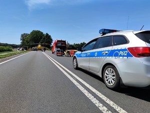 Zdjęcie kolorowe: na pierwszym plane widoczny oznakowany radiowóz w tle Lotnicze Pogotowie Ratunkowe i wozy straży pożarnej.