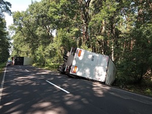 Zdjęcie kolorowe: wywrócony pojazd ciężarowy wraz z przyczepą na jezdni.