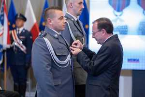 Zdjęcie kolorowe: dwóch umundurowanych policjantów. Jednemu z nich mężczyzna w garniturze przypina medal do gabardyny policyjnej.