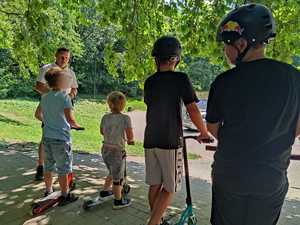 Zdjęcie kolorowe: umundurowany policjant podczas rozmowy z dziećmi w skateparku.