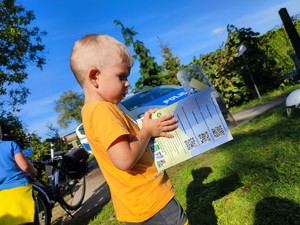 Zdjęcie kolorowe: mały chłopiec ogląda kolorowankę. W tle radiowóz.