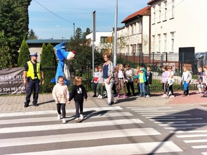 Zdjęcie kolorowe przedstawia ćwiczenie bezpiecznego przechodzenia przez pasy w obecności policjanta.