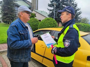 Zdjęcie kolorowe przedstawia umundurowanego policjanta wraz z mężczyzną podczas rozmowy.