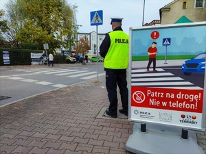 Zdjęcie kolorowe: umundurowany policjant obok plakatu informacyjnego.