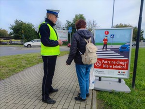 Zdjęcie kolorowe przedstawia umundurowanego policjanta który stoi na chodniku obok mężczyzny.