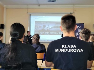 Zdjęcie kolorowe przedstawia uczniów klasy mundurowej podczas oglądania prezentacji dotyczącej doboru do służby w Policji.