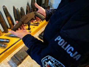 Zdjęcie kolorowe przedstawia zabytkowy pistolet w rękach policjanta.