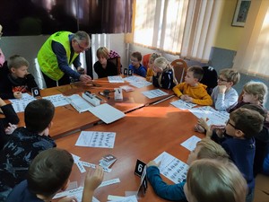 Zdjęcie kolorowe przedstawia policjanta, który pokazuje dzieciom jak się ściąga odciski palców.