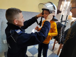 Zdjęcie kolorowe przedstawia policjanta, który zakłada dziecku na głowę policyjny kask.