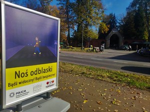 Zdjęcie kolorowe przedstawia kolorowy plakat przy drodze.