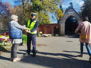 Zdjęcie kolorowe przedstawia policjanta ruchu drogowego który zakłada kobiecie odblask na rękę.