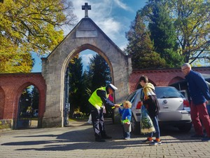 Zdjęcie kolorowe przedstawia policjanta ruchu drogowego który dziecku daje odblask.