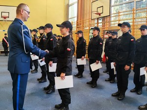 Zdjęcie kolorowe przedstawia  umundurowanego policjanta podczas składania gratulacji uczennicy klasy mundurowej.