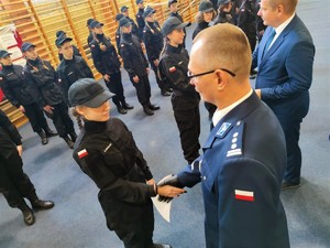 Zdjęcie kolorowe przedstawia  umundurowanego policjanta podczas składania gratulacji uczennicy klasy mundurowej.