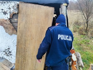 Zdjęcie przedstawia umundurowanego policjanta podczas kontroli prowizorycznego domku.