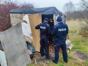 Zdjęcie przedstawia umundurowanych policjantów zaglądających do prowizorycznego szałasu.