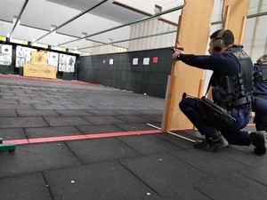 Zdjęcie przedstawia policjanta, który strzela z broni krótkiej na strzelnicy.