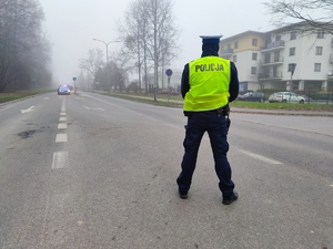 Zdjęcie przedstawia umundurowanego policjanta. Z tyłu widoczna orkiestra.