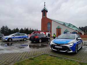 Zdjęcie przedstawia policyjne radiowozy i wóz straży pożarnej. Z tyłu widoczni strażacy, policjanci i Mikołaj.