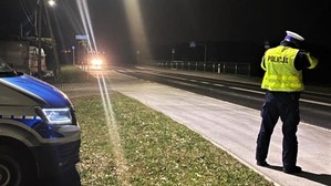 Zdjęcie przedstawia policjanta podczas pomiaru prędkości samochodów po zmroku.