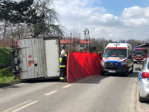 Zdjęcie przedstawia wywrócony samochód dostawczy oraz parawan zasłaniający miejsce zdarzenia.