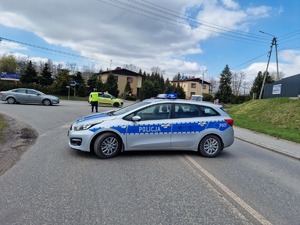 Zdjęcie przedstawia policyjny radiowóz oraz policjanta, który kieruje ruchem.