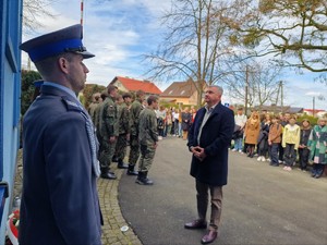 Zdjęcie przedstawia mężczyznę oddającego honor przed tablicą pamiątkową.