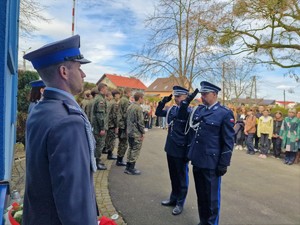 Zdjęcie przedstawia umundurowanych policjantów salutujących przed tablicą pamiątkową.