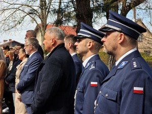 Zdjęcie przedstawieni są z przodu dwaj umundurowani policjanci, dalej widoczni zgromadzeni goście.