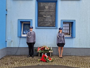 Zdjęcie przedstawia policjantów podczas warty honorowej przy tablicy pamiątkowej.