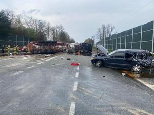 Zdjęcie przedstawia miejsce zdarzenia drogowego. Widoczny uszkodzony samochód osobowy oraz cysterna, które leże w poprzek drogi.