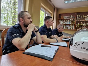 Zdjęcie przedstawia: policjantów siedzących przy stole z notatnikami służbowymi.