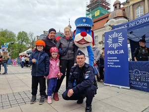 Zdjęcie przedstawia: rodzinę z dziećmi, Sznupka i umundurowanego policjanta podczas zdjęcia pozowanego.