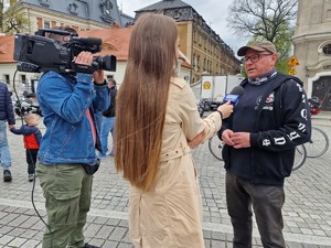 Zdjęcie przedstawia: mężczyznę podczas wywiadu. Obok mężczyzny kobieta z mikrofonem i mężczyzna z kamerą.