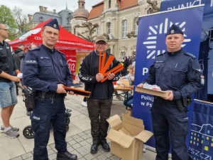 Zdjęcie przedstawia: policjantów wraz z mężczyzną. Wszyscy trzymają w rękach odblaski, przed mężczyzną stoi wielki karton.