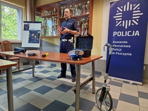 Zdjęcie przedstawia: umundurowanego policjanta Wydziału Ruchu Drogowego. Przed mundurowym na stole leżą urządzenia pomiarowe drogówki.
