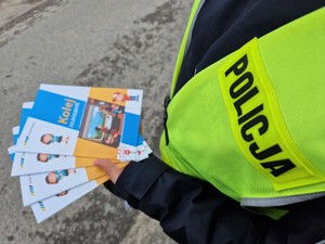 Zdjęcie przedstawia: kolorowanki, które trzyma w ręce policjant.