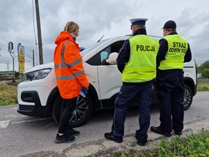 Zdjęcie przedstawia: policjant, funkcjonariusz Straży Ochrony Koli, kobieta w kamizelce odblaskowej przy zatrzymanym samochodzie.