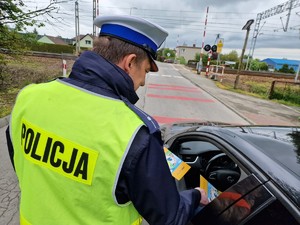 Zdjęcie przedstawia: umundurowanego policjanta podczas wręczania kolorowanek kierowcy samochodu.