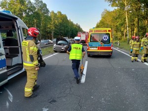 Zdjęcie przedstawia: policjanta drogówki podczas czynności na miejscu wypadku drogowego.